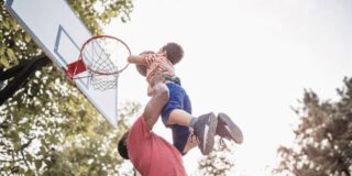 A man lifts a child up to dunk a basketball into a hoop.