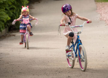 Two little girls riding their bikes with big smiles on their faces.