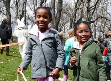 Two little girls with big smiles on their faces at an egg hunt.