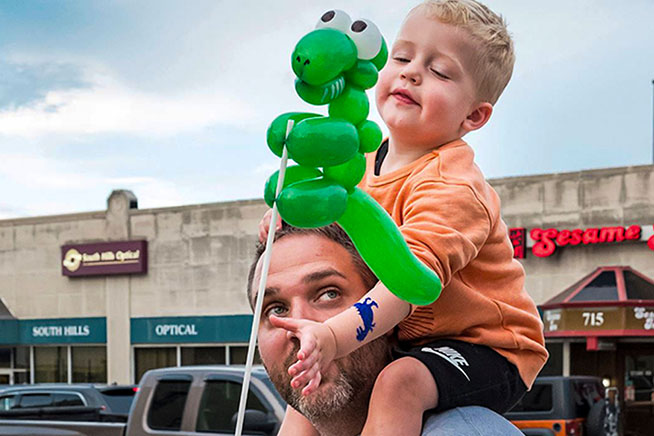 A boy holding a balloon sits on a man's shoulders.