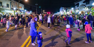 A crowd of adults and kids dressed in winter coats and hats lines Beverly Road during Beverly Brite Nite. It's dark and the street is lit by the lamps.