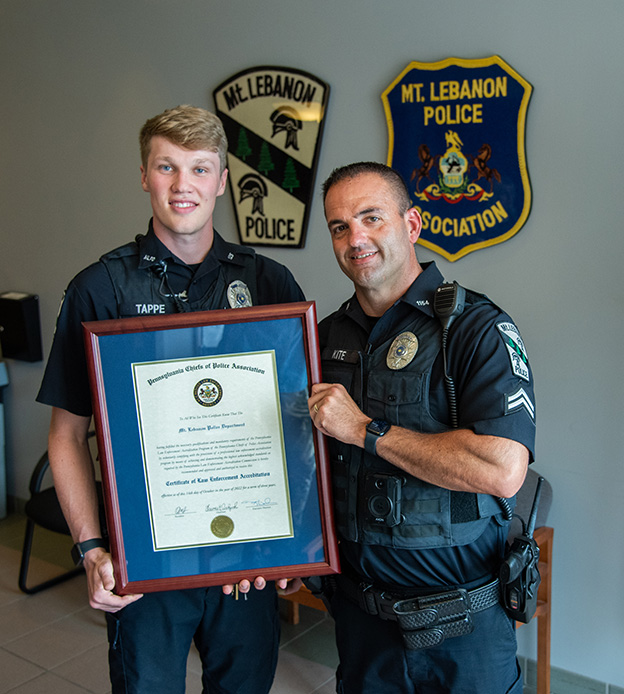 Two police officers holding an accreditation plaque