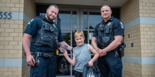 Two male police officers stand with a child who is holding up trading cards