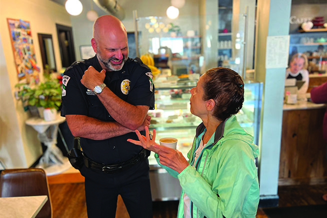 Picture of a tall police officer chatting with a woman in a green jacket at a coffee shop