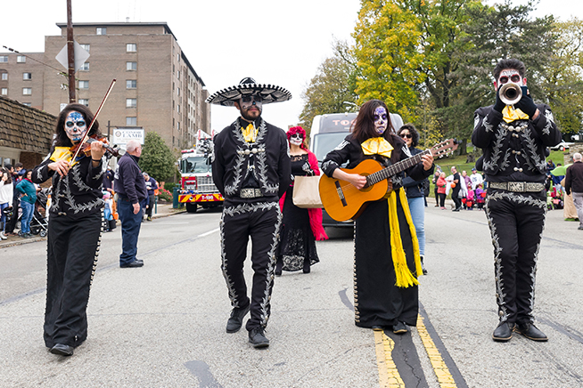 Four musicians dressed in sugar skull costumes marching in a Halloween parade.