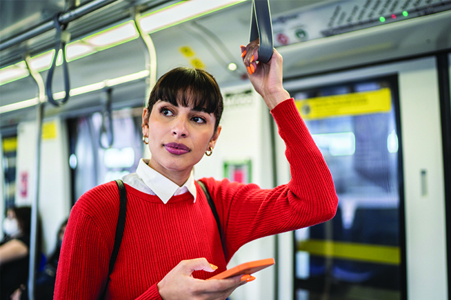 A woman in a red sweater using a cell phone rides on a subway car
