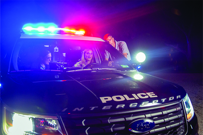 Police officer talking to a couple who are sitting inside a car