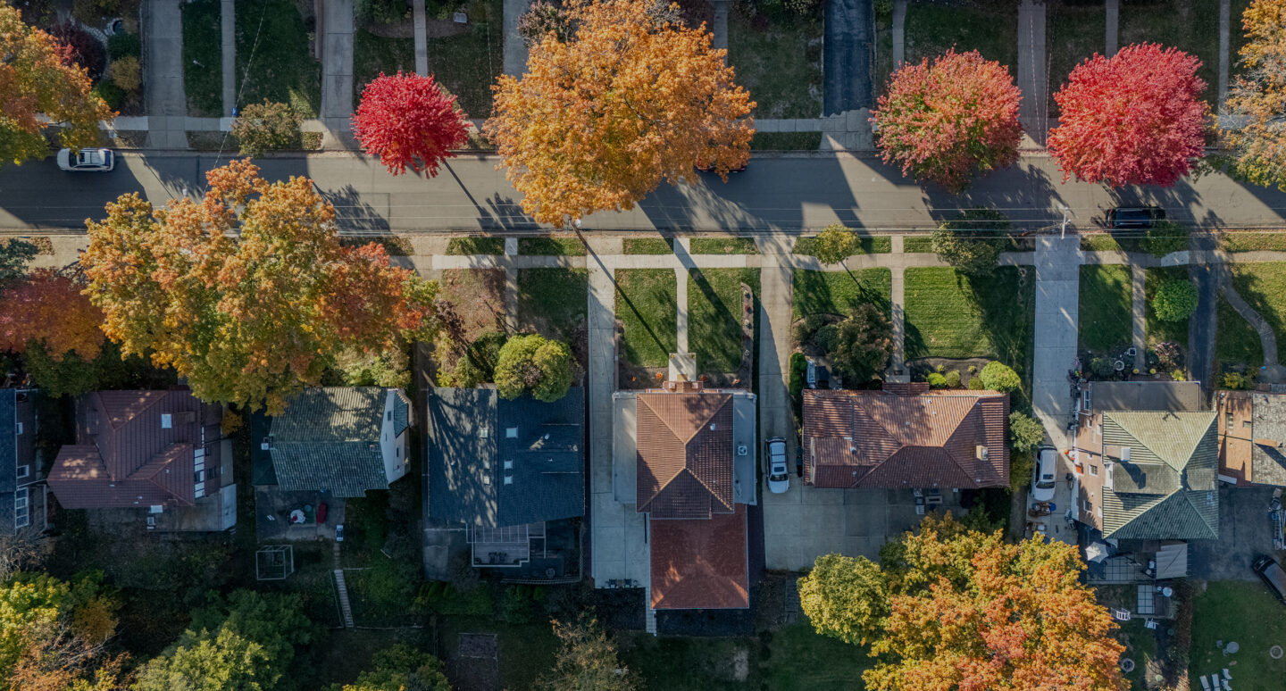 Aerial view of a suburban street with colorful autumn trees lining the sidewalk.